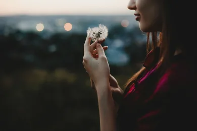 Female portrait. Nature. Pretty woman plays with dandelion standing before the sunset view